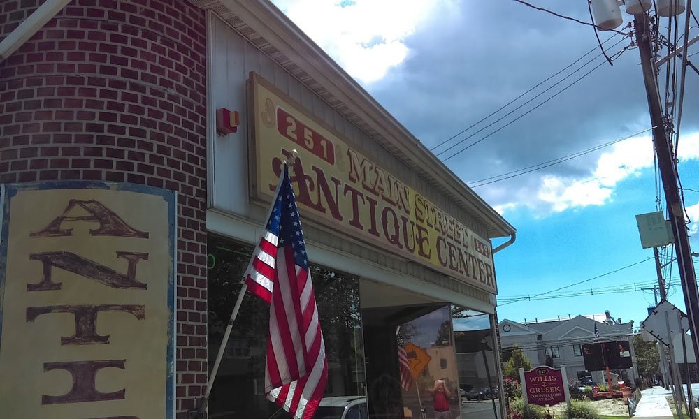 A brick antique shop with a large sign reading “251 Main Street Antique Center” and an American flag at the entrance, under a partly cloudy sky—one of the unique things to do in Ocean County NJ.