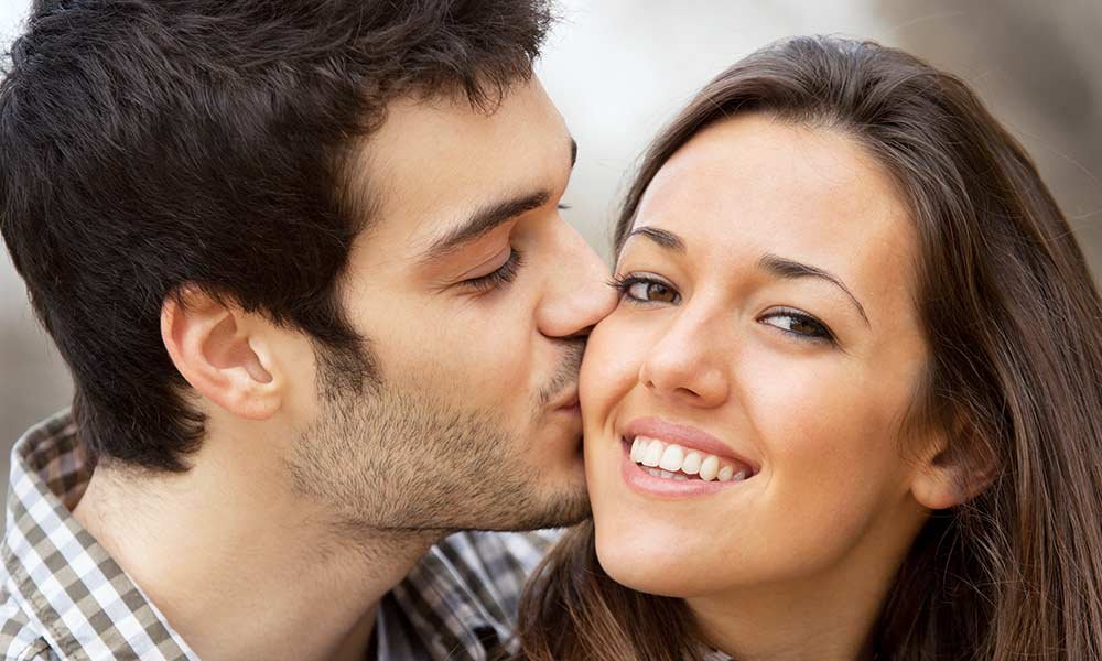A man kisses a smiling woman on the cheek outdoors, both appearing happy in casual clothing as they enjoy their time together—perhaps while exploring bed and breakfast packages in Toms River, NJ.